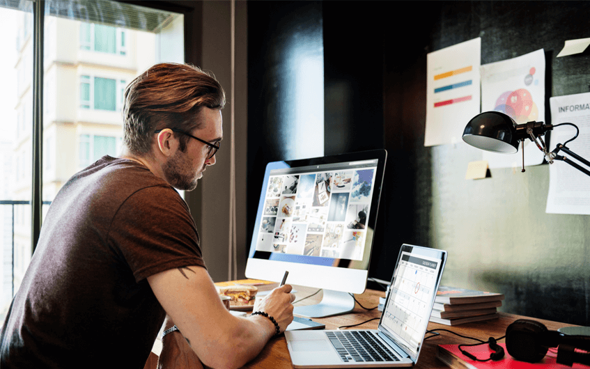 Homem trabalhando em casa com dois computadores - Home Office