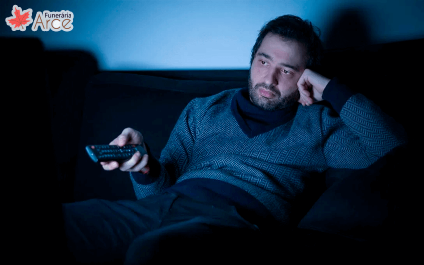 Homem entediado sentado no sofá assistindo televisão - sedentarismo